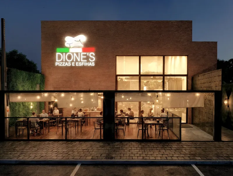 Fachada noturna do restaurante Dione's Pizzas e Esfihas com iluminação e área de mesas - Projeto comercial Arquiteta Melissa